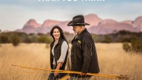 image of woman with Aboriginal guide holding spearks and walking through long grass