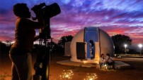 sunset image with woman looking through telescope and couple sitting in front of dome